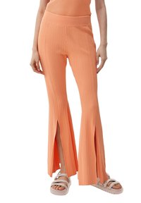 Perzikkleurige, geribbelde flared broek met zijsplitten, voorzien van een brede tailleband en een zachte textuur, gecombineerd met lichtgekleurde sandalen.