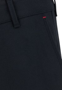 Granatowy denim o gładkiej fakturze, z delikatnym diagonalnym splotem, z czerwonym akcentującym przeszyciem w okolicy pasa i starannie wykończonymi szwami.