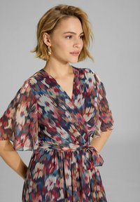 Robe portefeuille en tissu léger et fluide avec un motif abstrait multicolore en rouge, bleu et crème. Dotée de manches courtes et flottantes et d'une ceinture.