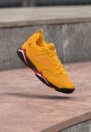 Baskets de sport jaunes et noires avec des accents rouges, en l'air au-dessus d'une surface en pierre, avec des détails visibles en mesh et lacets.