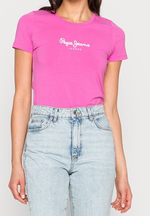 Vrouw draagt een felroze Pepe Jeans London t-shirt, ingestopt in lichtblauwe jeans met een hoge taille tegen een egale achtergrond.