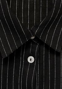 Maglietta a strisce nere con linee verticali bianche, colletto classico e un bottone bianco rotondo sulla patta del colletto. Tessuto testurizzato.