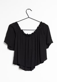 Svart kortärmad blus med lös passform, strukturerad tyg, volangkrage och ojämn fåll, hängande från en svart krok.