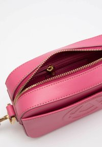 Borsa in pelle rosa con chiusura a zip, dotata di accessori in oro, una texture liscia e un logo in rilievo sul davanti.