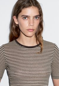 Pruhovaný pletený top se střídajícími hnědými a krémovými proužky, žebrovaným výstřihem a přiléhavým střihem.