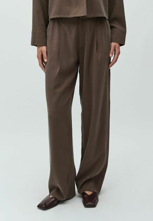 Brązowe, lekkie spodnie o szerokich nogawkach i gładkiej fakturze. Posiadają przednie zakładki i luźny krój, zestawione z ciemnoczerwonymi, bordowymi butami wsuwanymi.