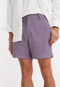Shorts din corduroy de culoare violet deschis, având buzunare laterale, sistem pentru curea și un tiv care se termină deasupra genunchiului. Stilizat cu o cămașă albă cu nasturi.