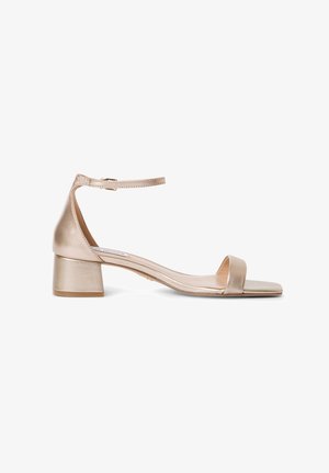 Sandalia de tacón metálica dorada con tacón ancho, punta descubierta, correa en el tobillo y textura suave. Presenta un diseño minimalista con una silueta esbelta.