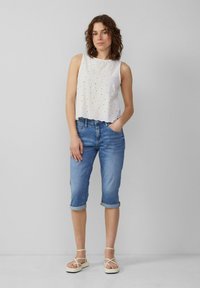 Haut sans manches blanc avec un motif en œillets, jean cropped bleu et sandales légères. Le tissu semble léger ; design globalement décontracté.