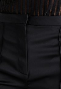 Schwarze Hosen mit glatter Satin-Oberfläche, ausgestattet mit einem schlichten Bund, frontalen Taschen und minimalem Nähedetail für einen maßgeschneiderten Look.