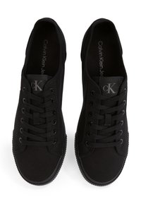 Mustade Calvin Kleini madala säärega lõuendist tossude paar, millel on mustad paelad, metallist silmad ja logo keelel ning sisetallal, nähtud ülalt.