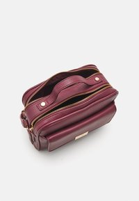 Borsa a mano in pelle bordeaux con superficie texturizzata, doppi zip e manico superiore. Presenta un accento in metallo dorato sulla parte anteriore.