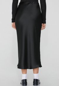Schwarzer Satin-Midi-Rock mit glatter Textur, tailliertem Bund und leichter Ausweitung am Saum. Trägt schwarze Schuhe und weiße Socken.