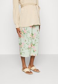 Saia midi floral em verde claro com um padrão de flores rosas e amarelas. Combinada com sandálias de slide bege, com um design de duas faixas.