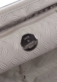 Borsa per scarpe e biancheria in tessuto grigio chiaro con motivo a onde; presenta un'etichetta circolare che recita "BORSA PER SCARPE E BIANCHERIA". Chiusura con zip.