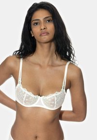 Biała półprzezroczysta biustonosz z kwiatowym haftem, koronkowym wykończeniem i regulowanymi ramiączkami. Posiada falbaniasty dekolt i wsparcie w postaci fiszbin.