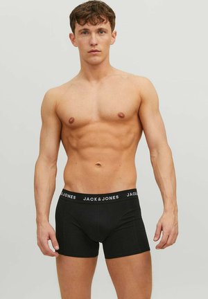 Young muscular man with short brown hair wearing black Jack & Jones boxer briefs standing against plain light background.