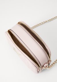 Pink leather crossbody bag with quilted texture, dual zip compartments, gold-tone hardware, and a chain strap. Inside features a brown lining.