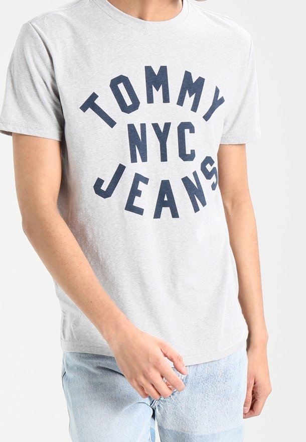 Harmaa puuvillapaita, jossa on voimakkaat tummansiniset tekstit "TOMMY NYC JEANS". Lyhyet hihat ja tavanomainen pyöreä kaula-aukko.