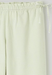 Pantalons à carreaux vert clair avec une taille élastique et un cordon de serrage noué. Le tissu a une texture douce et un motif à petits carreaux subtil.