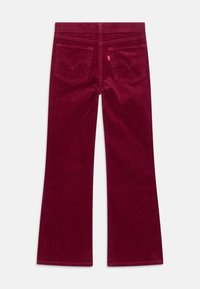 Burgundin väriset samettihousut, joissa on leveä lahje, takataskut, ommellut yksityiskohdat ja sileä pinta, jossa on hienovarainen raidoitus.