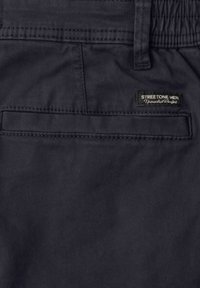 Gros plan sur la poche arrière d'un pantalon bleu marine foncé avec une étiquette "Streetone Men Unmatched Comfort" et une boucle de ceinture au-dessus.