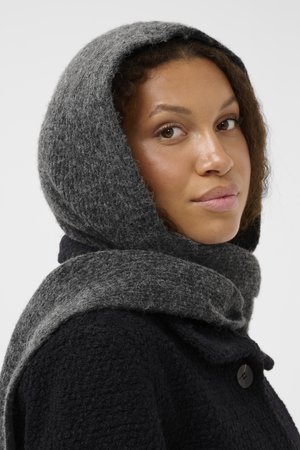Gray knitted hood scarf drapes over shoulders, paired with a dark textured coat. Features a soft and warm appearance with subtle patterns.