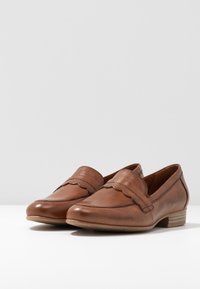 Mocassins en cuir marron avec un design festonné à l'avant, bout rond et petit talon empilé. Texture lisse et détails de couture minimalistes.