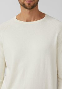 Heller cremefarbener Pullover mit langen Ärmeln aus weichem, gestricktem Material. Verfügt über einen abgerundeten Halsausschnitt und Raglan-Schulternähte mit dezenten Steppnähten.