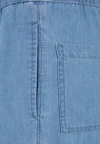 Džínový top světlé modré barvy s bočním rozparkem a náprsní kapsou. Měkká textura s viditelným šitím a stažením v pase.