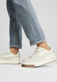 Sneakers color crema in pelle con finitura testurizzata, dotate di una suola in gomma spessa e dettagli di design minimalisti.