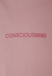 Różowy bawełniany t-shirt z wyraźnym, ciemnoróżowym napisem „CONSCIOUSMIND” w czystej, bezszeryfowej czcionce.