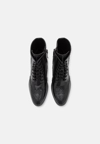 Bottines en cuir verni noir avec lacets et fermeture éclair sur le côté. Présentent des détails de brogue avec perforations et accents texturés.