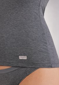 Szary bawełniany top na ramiączkach o dopasowanym kroju, z widoczną metką przy hemie z logo "Intimissimi". Bielizna w dopasowanym szarym kolorze jest częściowo widoczna.