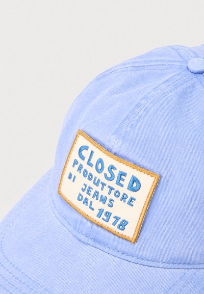 Γαλάζιο καπέλο με μπεζ πλακέτα που περιγράφεται με καφέ, με μπλε κείμενο που γράφει "CLOSED PRODUTTORE DI JEANS DAL 1978."