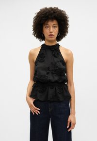 Melnā halter blūze ar ziedu izšuvumu, viļņotu apakšmalu un teksturētu audumu. Apvienota ar tumši ziliem džinsiem.