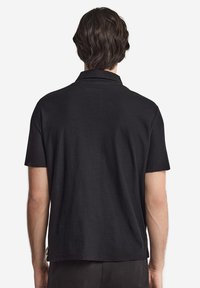 Svart pikétröja med avslappnad passform, korta ärmar och krage. Tyget har en subtil textur och en rak fåll.