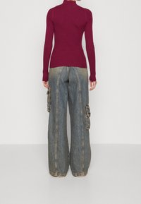 Burgundský žebrovaný rolák v kombinaci s volnými cargo džíny v bledě modrém denimovém provedení. Džíny mají boční kapsy a detaily šití.