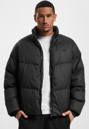 Chaqueta acolchada negra con cierre frontal, cuello alto y puños elásticos. Presenta secciones acolchadas y un logo sutil en el pecho.