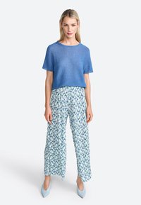 Top de punto de manga corta azul combinado con pantalones de pierna ancha de estampado floral en blanco, azul y verde. Acabado con zapatos de punta azul claro.