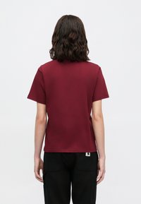 T-shirt bordeaux a maniche corte con collo tondo, realizzato in tessuto morbido, caratterizzato da un design semplice e senza decorazioni e da un taglio dritto sul retro.