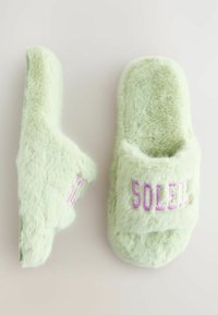 Vihreät tekoturkisliponit, joissa on pehmeä tekstuuri, avointo ja vaaleanliilalla brodeerattu "SOLEIL" nauhassa.