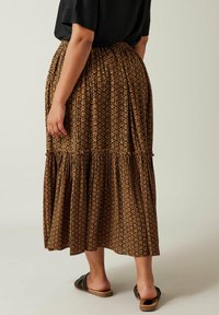 Bruine maxi rok met een patroon, met plooien, een gerimpelde zoom en een elastische tailleband, gecombineerd met zwarte platte sandalen.