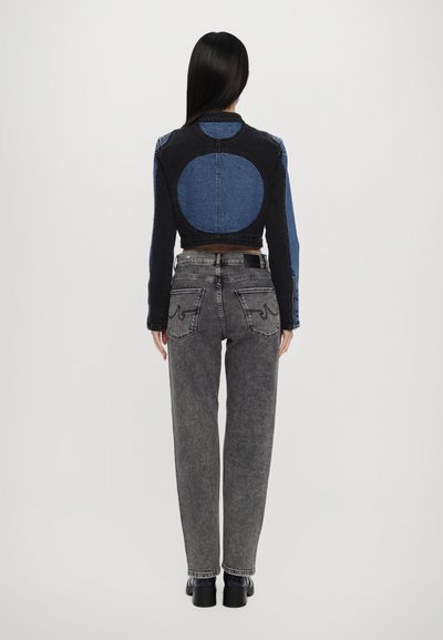 Cropped denim jacket with a circular blue patch on the back, paired with gray high-waisted jeans and black chunky boots.