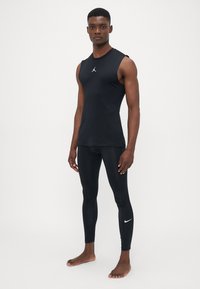 Zwarte mouwloze sporttanktop met een klein Jordan-logo, gecombineerd met zwarte leggings die een witte Nike swoosh hebben, beide gemaakt van een gladde stof.