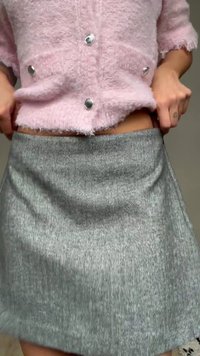 Personne ajustant une jupe grise à motif chevrons taille haute, portant un cardigan en maille pelucheuse rose avec des boutons argentés.