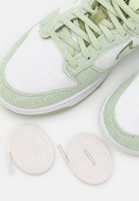 Baskets avec superposition textile verte et sections synthétiques blanches. Comportent des lacets verts texturés et deux lacets ronds blancs avec embouts.