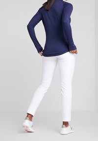 Mörkblå långärmad topp, vita åtsittande byxor och silverfärgade sneakers. Kläderna har en elegant design med en slät textur.