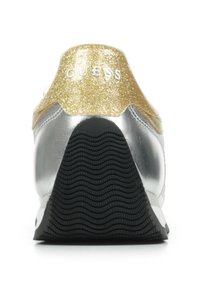 Zapatilla plateada con un talón de purpurina dorada, con una suela negra texturizada. Nombre de la marca "GUESS" grabado en el talón. Diseño elegante y forma moderna.