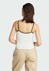 White sleeveless top with leopard print straps, featuring a fitted design. Paired with beige pants, showing a casual look from the back.